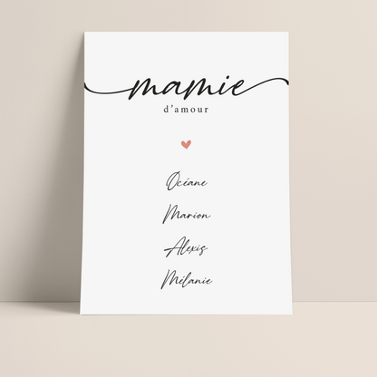 Photo d'une affiche graphique composé du titre "Mamie" en écriture scripte surmontant la mention "d'amour". En dessous se trouve un coeur rose presqu'au centre de l'affiche puis 4 prénoms, Océane, Marion, Alexis, Mélanie tous écrit en noir dans une police liée.